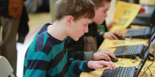 male student working on a computer, classmates in background